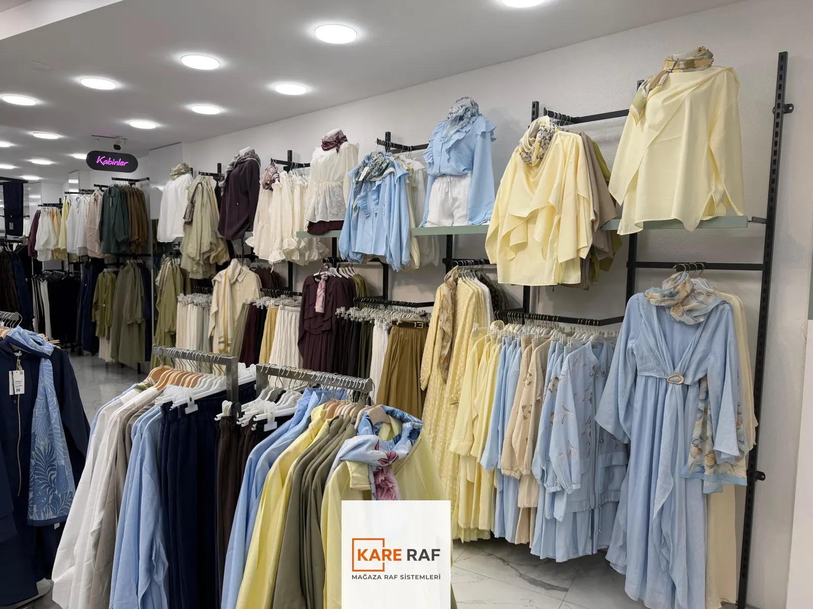 Armira mağazasında siyah dikmeli duvar askı sistemi, pastel tunik ve elbiseler, önde ayaklı askı